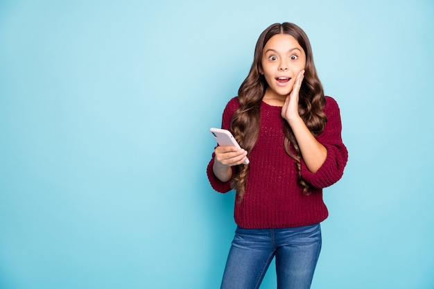 Foto de alegre gracioso escolar en jeans denim suéter borgoña sosteniendo teléfono