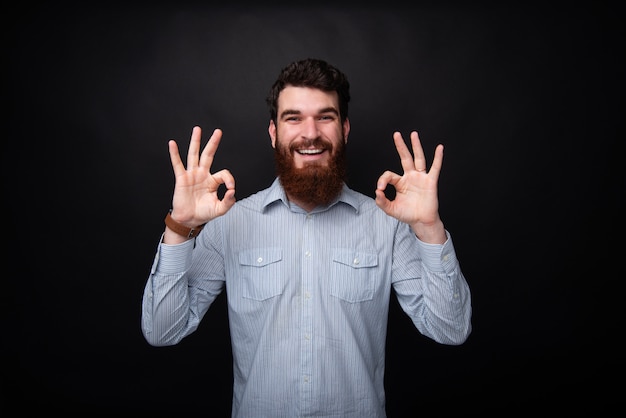 Foto de un alegre hombre barbudo mirando a la cámara mientras muestra un signo bien con ambas manos