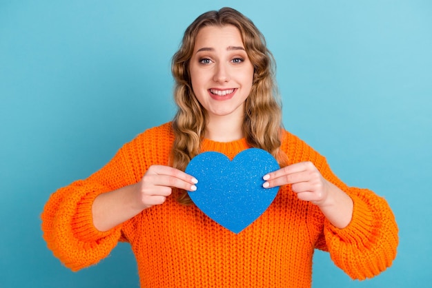 Foto de una alegre joven feliz que se toma de la mano con forma de papel de corazón azul aislada en un fondo de color azul