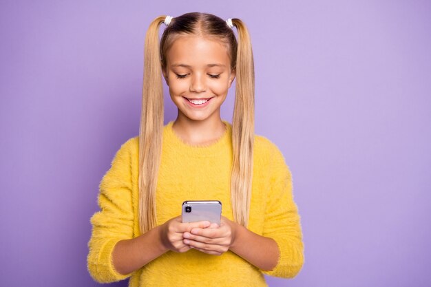 Foto foto de alegre linda chica positiva sonriendo toothily navegando por teléfono aislado sobre pared violeta de color pastel