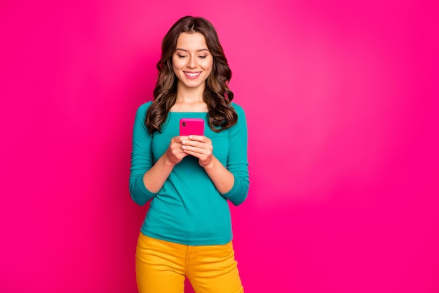 Foto de alegre novia positiva navegando a través del smartphone sonriendo toothily leyendo feednews aislado fondo de color rosa vivo