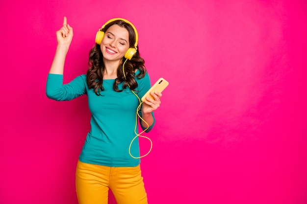 Foto de alegre positivo lindo agradable bastante encantadora chica bailando escuchando música con auriculares con pantalones pantalones amarillos aislados cerca del espacio vacío sobre fondo de color rosa vibrante
