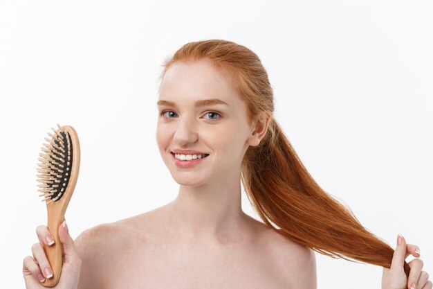 Foto de alegre sonriente pecosa jengibre joven peina su largo cabello rojo