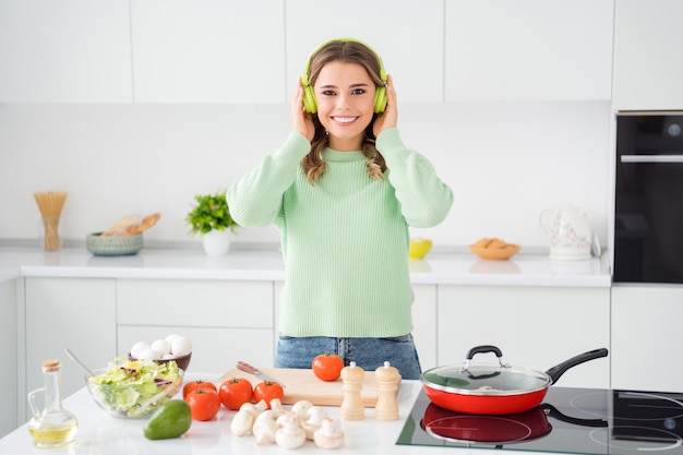 Foto de ama de casa alegre ensalada de corte cocinando cena sabrosa escuchar música