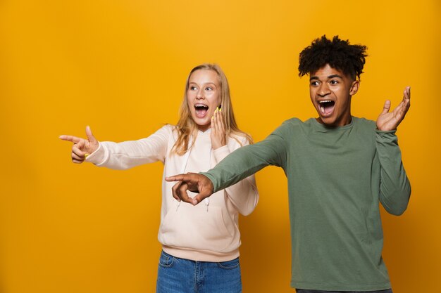 Foto de amigos adolescentes hombre y mujer de 16-18 con aparatos dentales riendo y señalando con el dedo a un lado en el copyspace, aislado sobre fondo amarillo