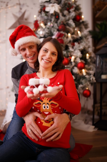 Foto de amoroso hombre y mujer embarazada con botines sobre fondo de adornos navideños en estudio