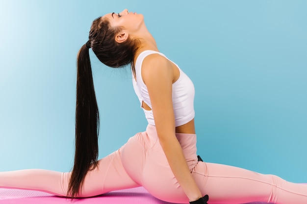 Foto ampliada. Una chica deportiva con una hermosa figura se enrosca en una colchoneta de fitness. Fondo azul