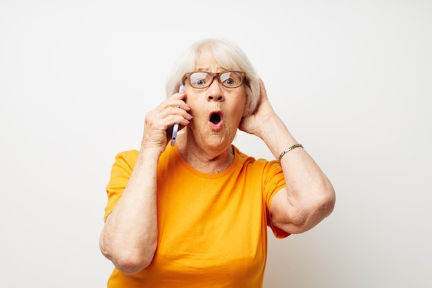 Foto de una anciana jubilada con gafas casuales de camiseta hablando por teléfono de fondo aislado