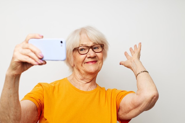 Foto de una anciana jubilada con gafas de moda con un teléfono inteligente en el fondo claro de la mano