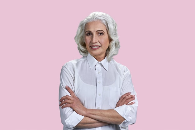 Foto de anciana pensionista con los brazos cruzados aislado sobre fondo de color rosa