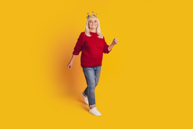 Foto de anciana positiva con corona de oro sobre fondo amarillo