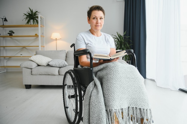 Una foto de una anciana sentada en una silla de ruedas y leyendo un libro en casa