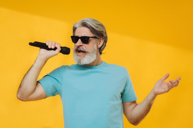 Foto de un anciano canoso cantando con gafas camiseta azul aislada de fondo amarillo