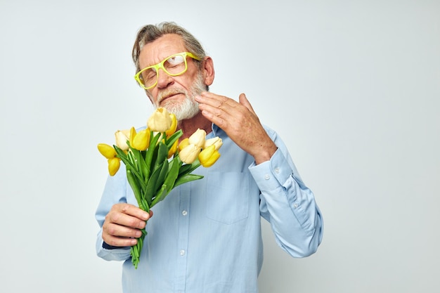 Foto de un anciano jubilado con una camisa azul con un ramo de flores de fondo claro