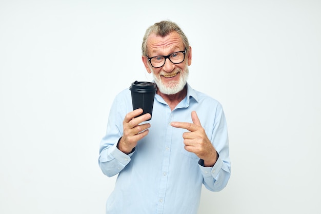 Foto de un anciano jubilado gesticula con las manos un vaso de bebida de fondo claro