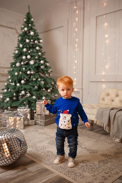 Foto de Año Nuevo de un niño pequeño cerca de un árbol de Navidad con regalos
