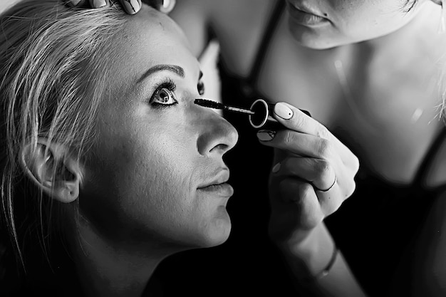 foto antigua en blanco y negro de una chica con maquillaje profesional / maquillaje estricto en la cara de una hermosa modelo profesional en un salón de belleza