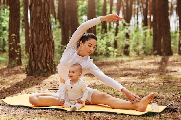 Foto ao ar livre da mãe e do bebê posando no karemat na floresta