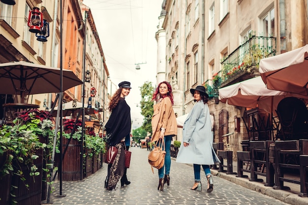 Foto ao ar livre de três mulheres caminhando na rua da cidade. Meninas virando e olhando para a câmera. Senhoras se divertindo