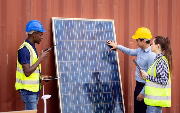 Foto ao ar livre de um engenheiro negro africano inspecionando painel solar elétrico usando capacete, óculos de proteção e equipamento de segurança,