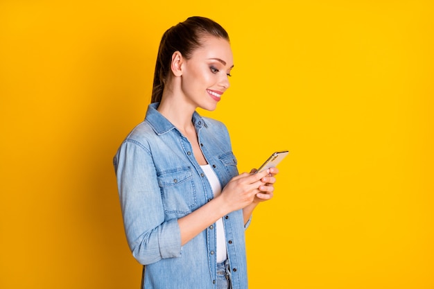 Foto ao lado do perfil da menina alegre positiva usar smartphone compartilhar repassar assinar rede social notícias vestir roupa estilo casual isolada sobre fundo de cor brilhante brilhante