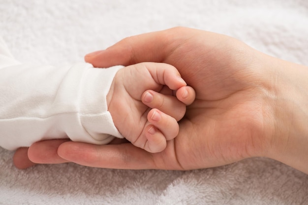 Foto aproximada da mão minúscula do bebê recém-nascido na palma da mãe sobre fundo têxtil branco isolado