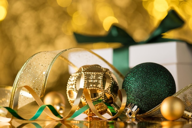 Foto aproximada de decorações de árvores de natal douradas e verdes ornamentos bolas de fita serpentina e caixa de presente branca sobre fundo dourado