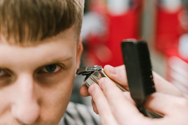 Foto aproximada de um cabeleireiro masculino aparando o cabelo com um aparador nas mãos