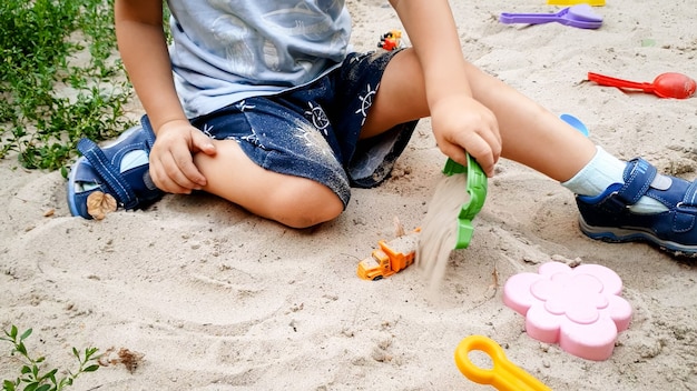 Foto aproximada de um menino de 3 anos brincando com o brinquedo na caixa de areia no parquinho