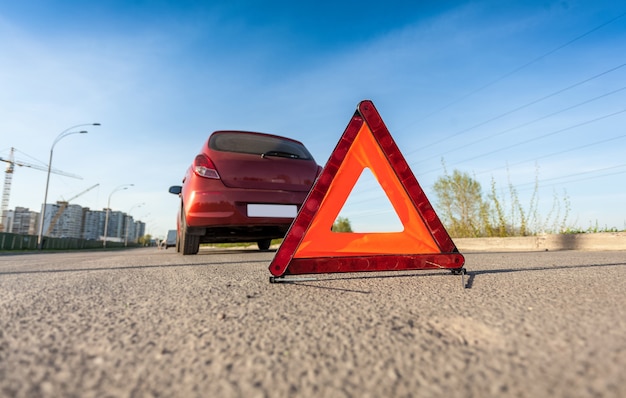 Foto aproximada de um triângulo vermelho na estrada ao lado de um carro quebrado