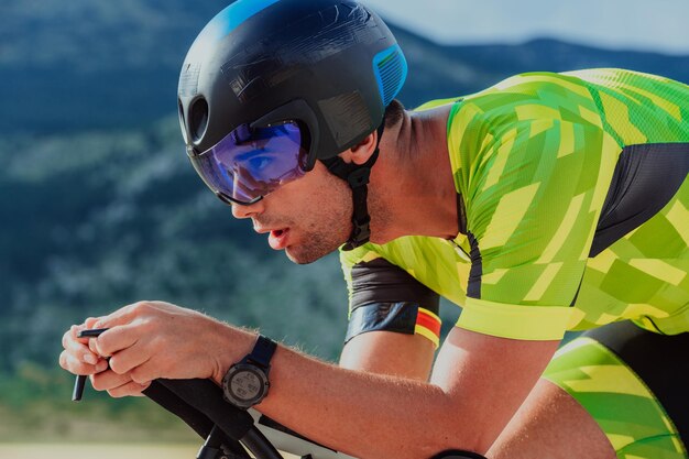 Foto aproximada de um triatleta ativo em roupas esportivas e com um capacete protetor andando de bicicleta. Foco seletivo.