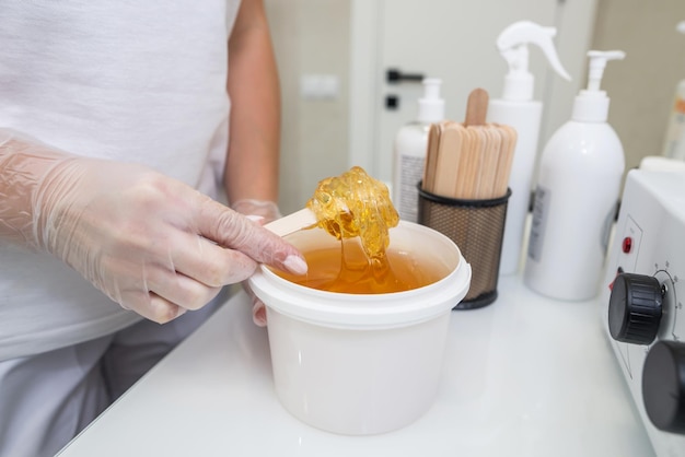 Foto aproximada de uma esteticista feminina com um balde de pasta de açúcar para um procedimento de depilação O conceito de depilação depilação depilação shugaring