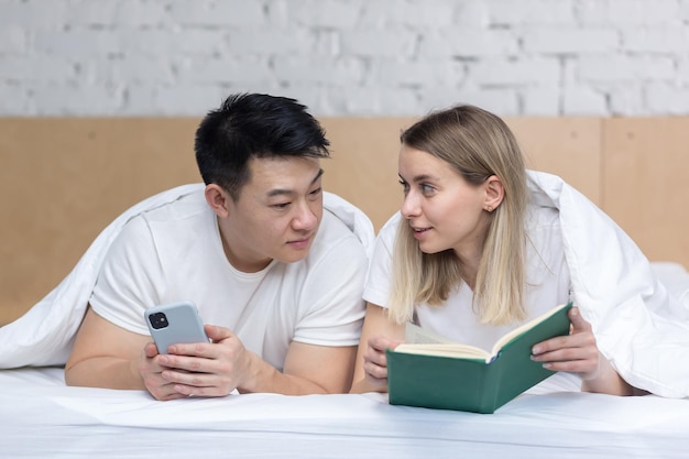 Foto aproximada de uma família feliz lendo um livro juntos deitado em uma cama debaixo de um cobertor homem e mulher casal feliz juntos