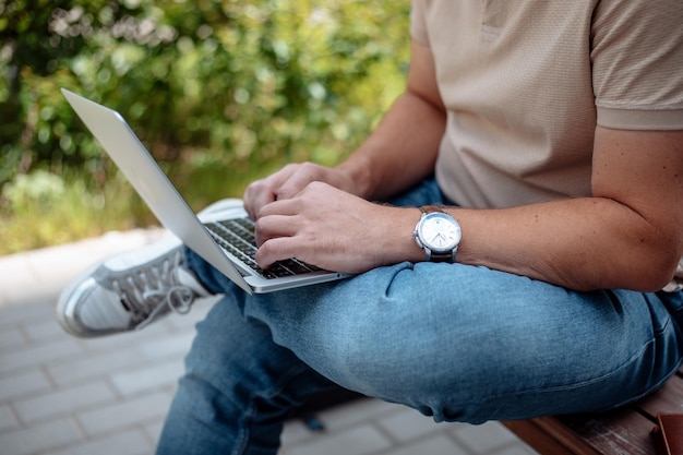 Foto aproximada do empresário sentado no banco no parque da cidade, trabalhando e digitando no laptop digital, foco seletivo, estilo de vida moderno, trabalho remoto, local de trabalho ao ar livre, conceito de tecnologia e pessoas