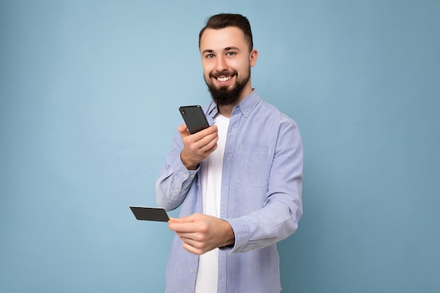 Foto de apuesto atractivo brunet sonriente joven sin afeitar vistiendo casual camisa azul y