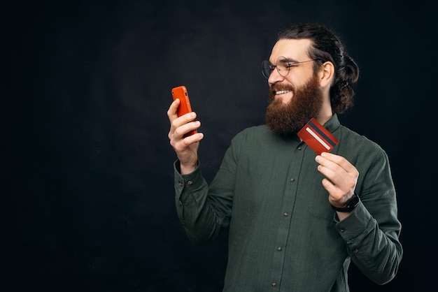 Foto de un apuesto joven con barba comprando en línea con tarjeta de crédito en un smartphone