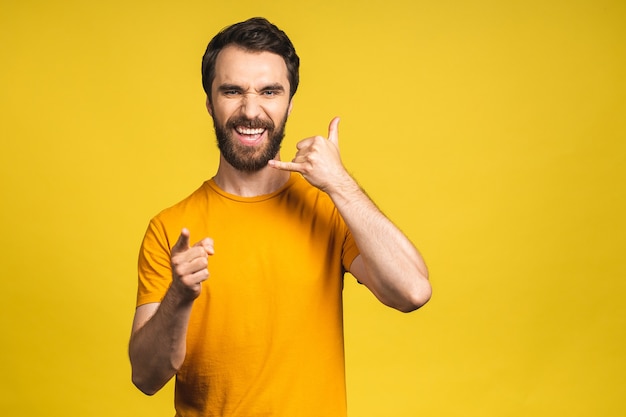 Una foto de apuesto joven barbudo en casual aislado sobre fondo amarillo haciendo un gesto de "llámame" con los dedos.