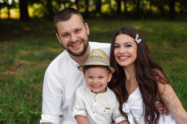 Foto de archivo en la cabeza de una hermosa familia caucásica de madre, padre y su hijo sonriendo felizmente a la cámara en el parque el día de verano.