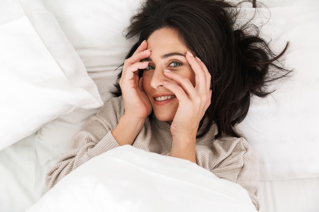 Foto desde arriba de una atractiva mujer de 30 años, sonriendo mientras está acostado en la cama en su casa