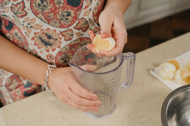 Una foto desde arriba de las manos de una mujer que está machacando jugo de limón con la mano en el vaso de la licuadora en la cocina.