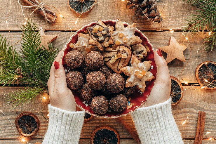 Foto de arriba de manos sosteniendo un plato de galletas de Navidad sobre tablas de madera con decoraciones