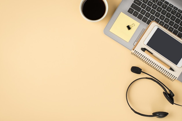 Foto de arriba de una taza de café gris para computadora portátil con un bolígrafo, clips de teléfono, auriculares y pegatinas aisladas en el fondo beige con espacio en blanco