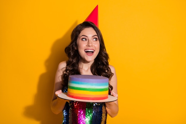 Foto de asombrada chica alegre positiva mirar copyspace sostener la torta de cumpleaños del arco iris imagina ocasión festiva vestimenta de fiesta cono rojo falda brillante aislado fondo de color brillante