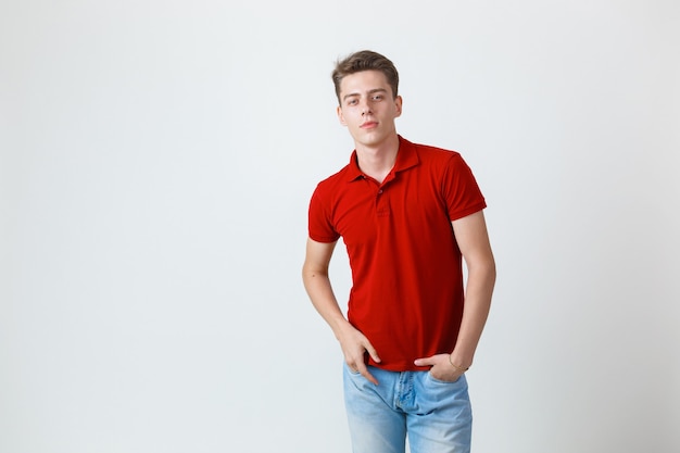 Foto de aspecto amable alegre chico europeo vistiendo camisa roja y jeans sonriendo