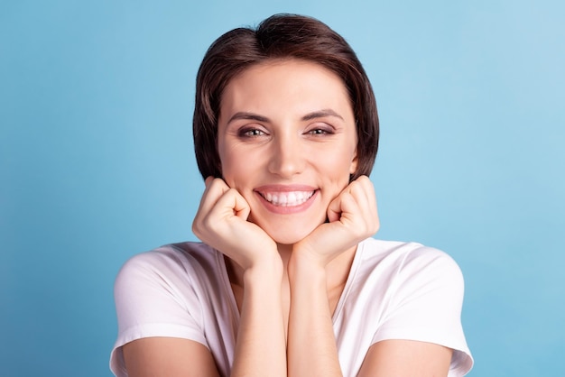 Foto de la atención de la clínica de los dientes de la barbilla del tacto de los brazos del buen humor de la mujer atractiva joven aislada sobre el fondo de color azul.