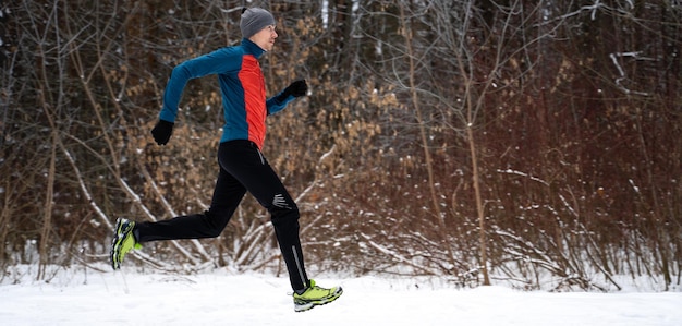 Foto de atleta corriendo entre árboles en el bosque de invierno