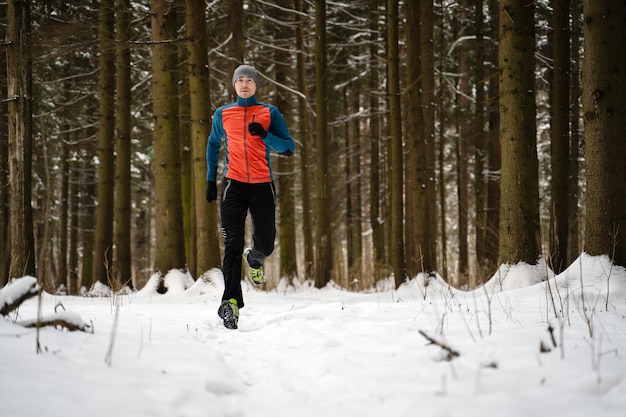 Foto de atleta corriendo entre árboles en el bosque de invierno