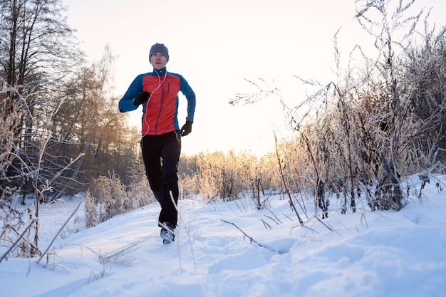 Foto de atleta corriendo entre árboles en el bosque de invierno