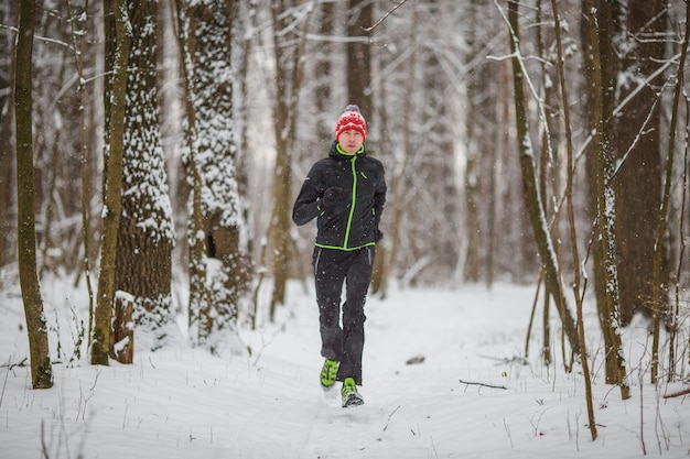 Foto de atleta corriendo entre árboles en el bosque de invierno