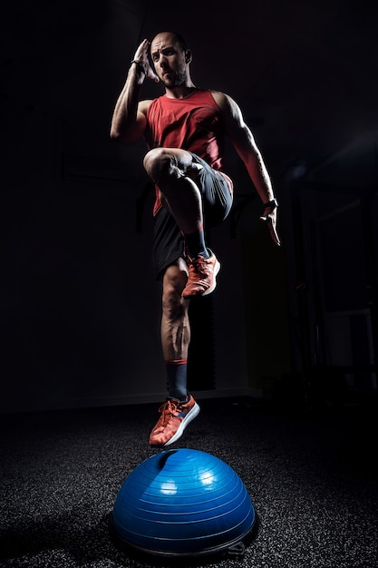 Foto de atleta en forma realizando ejercicio en bola bosu de hemisferio gimnástico en estudio oscuro.